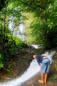 Full length of man standing by waterfall in forest