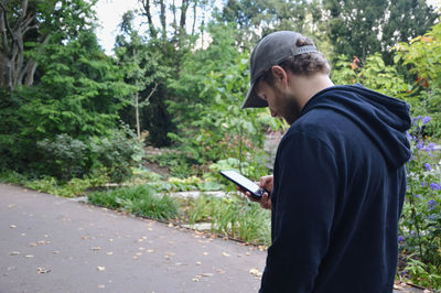 Man standing by trees and plants in park while being on his mobile phone texting