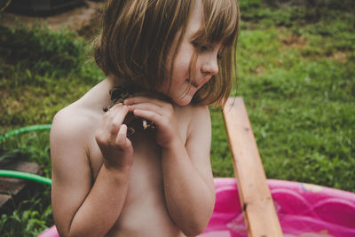 Midsection of shirtless girl holding plant in backyard