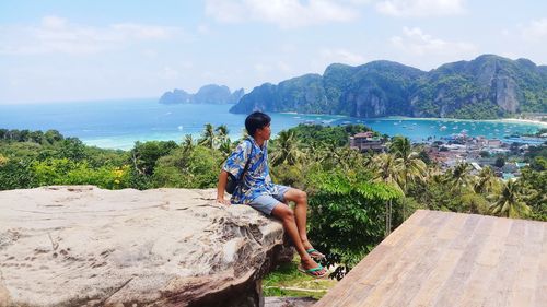 Man looking away while sitting on rock