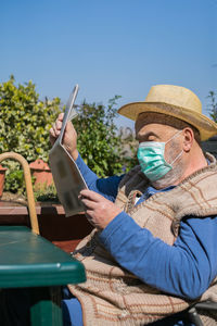 Midsection of man holding hat sitting against blue sky