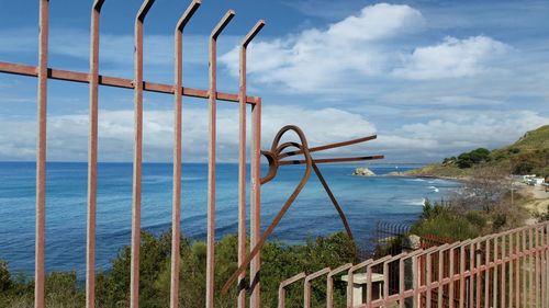 Metal railing by sea against sky 