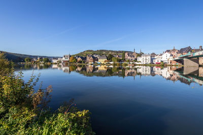 Buildings by river against clear blue sky