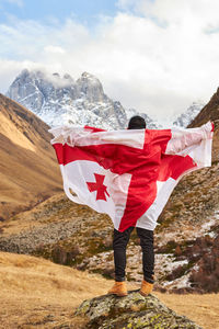 Back view of happy young man posing with georgia national flag standing outdoor 