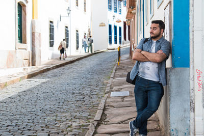 Young man leaning on wall by cobbled street in town