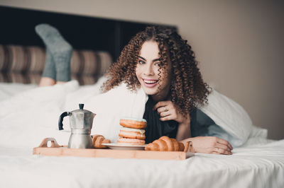 Portrait of happy woman lying by breakfast on bed at home