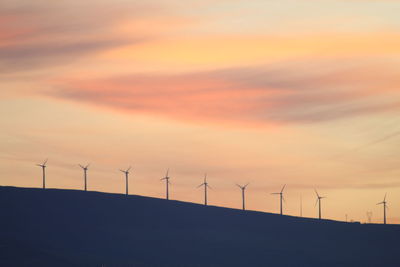 Silhouette wind turbines on land against sky during sunset