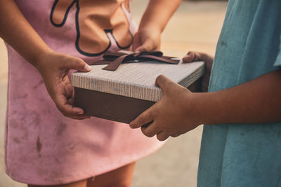 Midsection of friends holding gift box