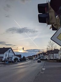 Road by buildings against sky during sunset