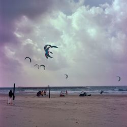 People on beach against cloudy sky