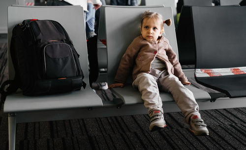 Bored tired child waiting at the airport, flight delay, girl sitting in lounge. big backpack luggage