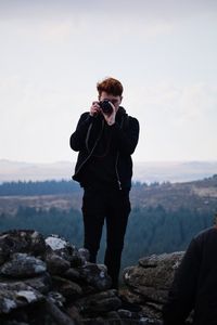 Man photographing on cliff against sky