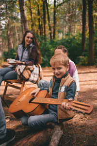 Happy family on a camping trip relaxing in the autumn forest. a boy holds a guitar in his hands.