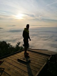 Man standing on wooden structure against cloudy sky