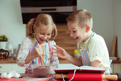 Cute sibling preparing food while reading recipe in book