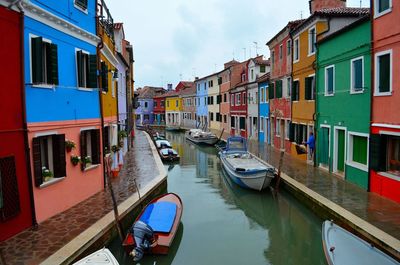 Boats moored in canal amidst buildings against sky