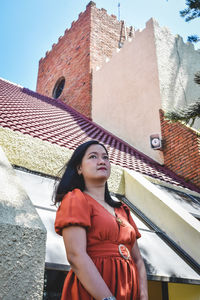 Portrait of young woman standing against building