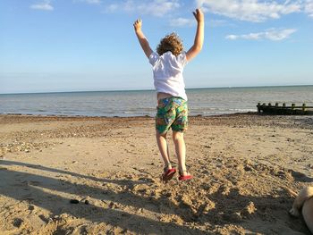 Rear view of boy jumping at beach against sky