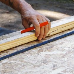 Cropped image of carpenter with pencil and wood working at construction site