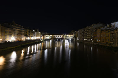 Illuminated bridge over river by buildings in city at night