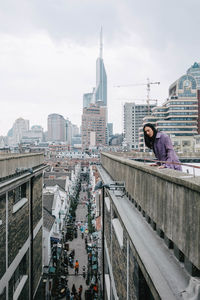 Woman amidst buildings in city against sky