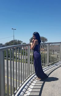 Woman standing on railing against blue sky