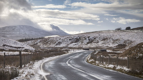 Road by snow covered mountains against sky