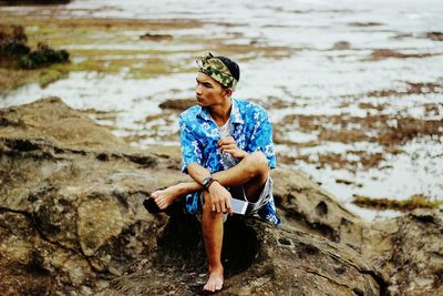 Full length of man sitting on rock at beach