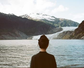 Rear view of woman standing in sea against mountains