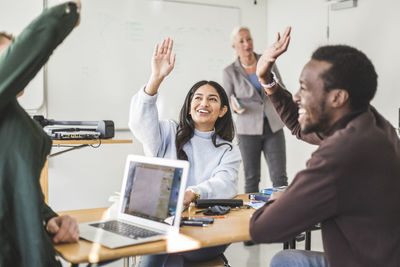 Smiling young woman and friends raising hands in classroom