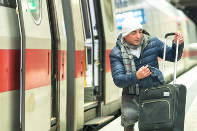 Man picking scarf from luggage at railroad station platform