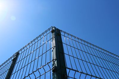 Low angle view of fence against building against clear blue sky