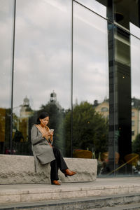 Full length of businesswoman using smart phone while sitting on bench