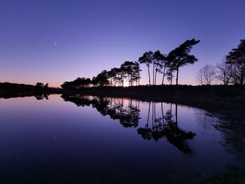 Silhouette trees by lake against sky during sunset