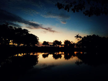 Silhouette trees by lake against sky during sunset