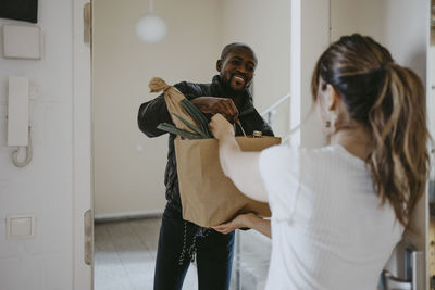 Smiling man giving paper bag of groceries to woman standing at doorway