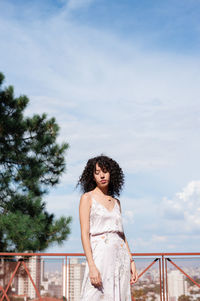 Portrait of woman standing by railing against sky