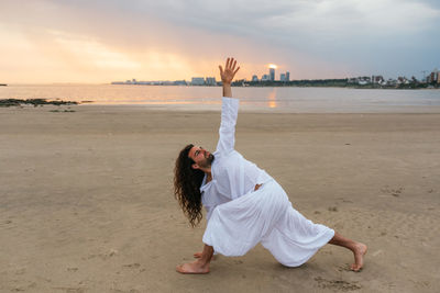 Stock photo of adult man with long hair doing yoga poses in the beach.