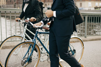 Midsection of businessman and businesswoman walking with bicycles on bridge in city