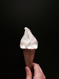 Cropped hand holding ice cream against black background