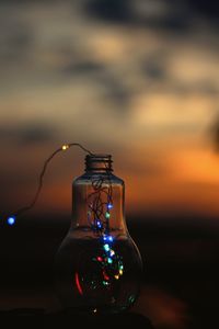 Close-up of illuminated bottle against sunset sky