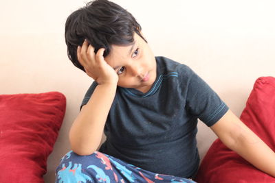 Cute disappointed boy sitting against white wall at home