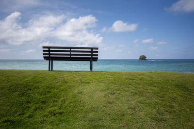 Empty bench on shore by sea against sky