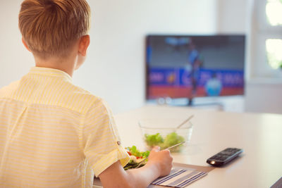 Rear view of boy eating breakfast at home