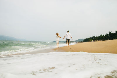 Rear view of couple walking on beach against clear sky