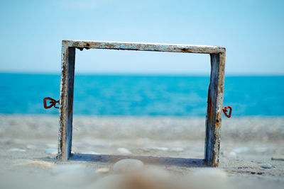 Close-up of rusty metal on beach against clear blue sky