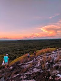 Rear view of people hiking on mountain against sky during sunset