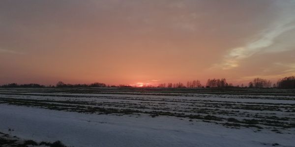 Scenic view of snowy field against sky during sunset