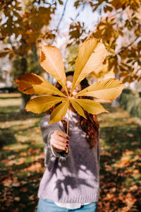 Midsection of person holding yellow flowering plant during autumn