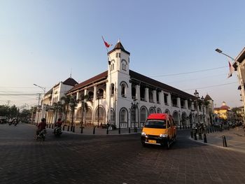 Cars on street by buildings against sky in city